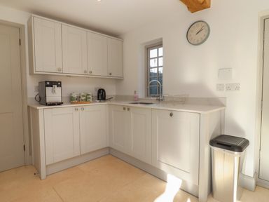 A kitchen with white cabinets a coffee machine a kettle a sink a clock and a trash bin at Blossom Cottage in Chipping Campden