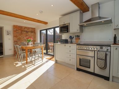 A kitchen with a stove microwave dining table chairs and a sliding glass door at Blossom Cottage in Chipping Campden