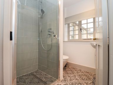 A bathroom with a glass shower enclosure and patterned floor tiles at Blossom Cottage in Chipping Campden