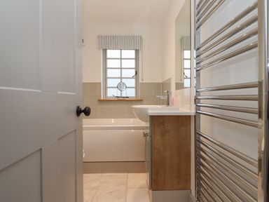 A bathroom with a bathtub sink mirror window and towel radiator at Blossom Cottage in Chipping Campden