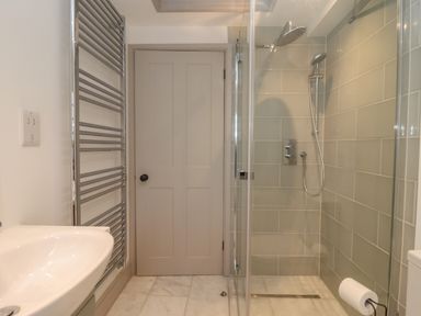 A bathroom with a shower enclosure a sink a towel radiator and a door at Blossom Cottage in Chipping Campden