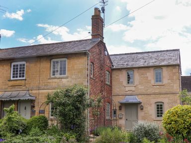 A stone and brick exterior of a cottage with garden and bushes at Blossom Cottage in Chipping Campden
