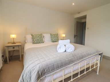 A bedroom with a bed with gray quilt and rolled white towels on top at Blossom Cottage in Chipping Campden