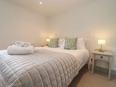 A bedroom with a bed with gray quilt green pillows and bedside tables with lamps at Blossom Cottage in Chipping Campden