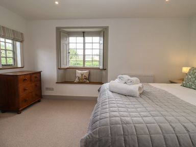 A bedroom with a bed covered in a quilt and towels on top next to a wooden dresser and a window seat at Blossom Cottage in Chipping Campden