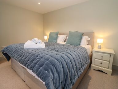 A bedroom with a bed covered in a quilted blanket two pillows and rolled towels on the bed with a bedside table and lamp at Blossom Cottage in Chipping Campden