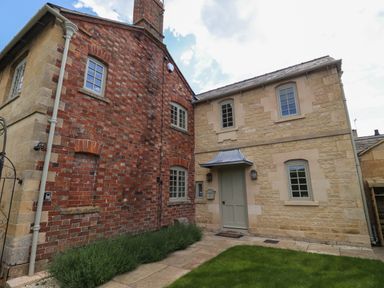 The exterior of a house with red brick and stone walls a green door and several windows at Blossom Cottage in Chipping Campden