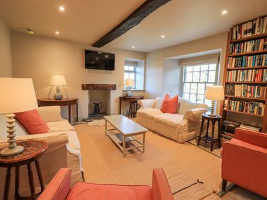A living room with sofas, armchairs, lamps, a coffee table, bookshelves, and a wall-mounted TV at Green Yew in Winster near Bowness-On-Windermere