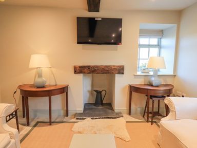 A living room with a wall-mounted TV above a fireplace flanked by two wooden tables with lamps at Green Yew in Winster near Bowness-On-Windermere