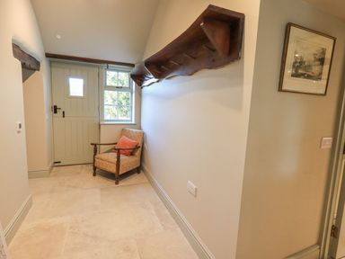 An entryway with a wooden chair with cushions near a door and window and a wooden shelf on the wall at Green Yew in Winster near Bowness-On-Windermere