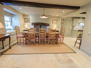 A dining room with a wooden table and six chairs with red cushions a window seat and a fireplace at Green Yew Winster near Bowness-On-Windermere