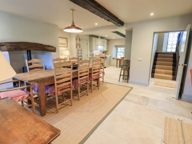A dining area with a large wooden table and chairs next to a kitchen and a staircase at Green Yew in Winster near Bowness-On-Windermere