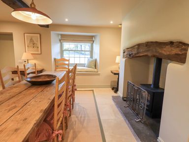 A dining room with a wooden table and chairs a window seat and a wood burning stove at Green Yew in Winster near Bowness-On-Windermere