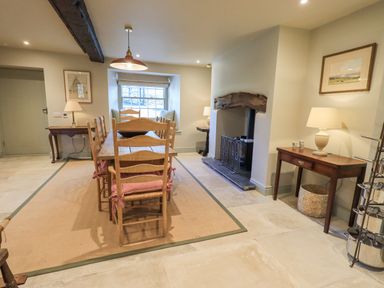 A dining room with a wooden table and chairs on a rug next to a fireplace and side tables at Green Yew in Winster near Bowness-On-Windermere
