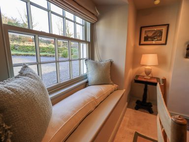 A window seat with cushions next to a small table with a lamp and framed picture at Green Yew Winster near Bowness-On-Windermere
