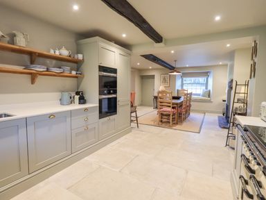 A kitchen and dining area with wooden chairs around a table and open shelves with dishes at Green Yew in Winster near Bowness-On-Windermere