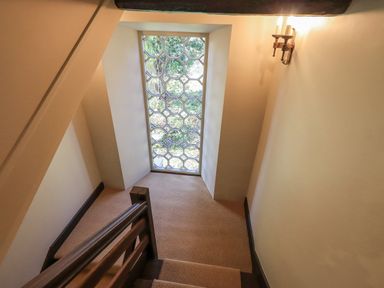 A stairway landing with a large decorative window and a wall light at Green Yew in Winster near Bowness-On-Windermere