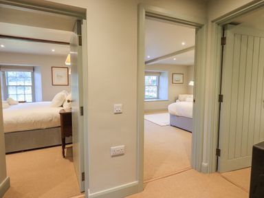 A corridor with two open doors leading to bedrooms with beds and windows at Green Yew in Winster near Bowness-On-Windermere