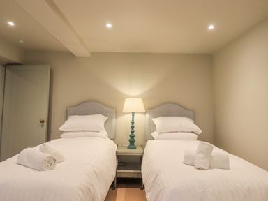 A bedroom with two single beds each with white bedding and towels with a lamp on a nightstand in the middle at Green Yew in Winster near Bowness-On-Windermere