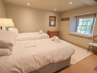 A bedroom with two single beds a wooden chest of drawers a window with a cushion and a wooden chair at Green Yew in Winster near Bowness-On-Windermere