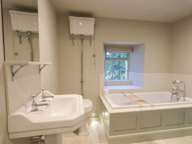 A bathroom with a bathtub under a window a toilet with a high-level cistern and a sink with separate taps at Green Yew in Winster near Bowness-On-Windermere