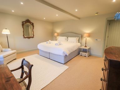 A bedroom with a large bed and bedside tables with lamps a wooden chair and desk a white armchair and a decorative mirror on the wall at Green Yew in Winster near Bowness-On-Windermere
