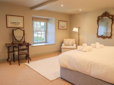 A bedroom with a bed, armchair, dressing table with mirror, framed pictures, and a window at Green Yew in Winster near Bowness-On-Windermere