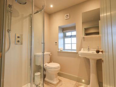 A bathroom with a glass shower, toilet, sink with a mirror, and a window at Green Yew in Winster near Bowness-On-Windermere