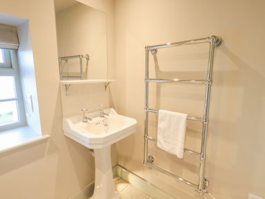 A bathroom with a pedestal sink mirror and heated towel rail with towel at Green Yew in Winster near Bowness-On-Windermere