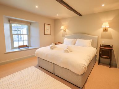 A bedroom with a large bed with white bedding and two rolled towels on it two wooden bedside tables and a window with a view at Green Yew in Winster near Bowness-On-Windermere