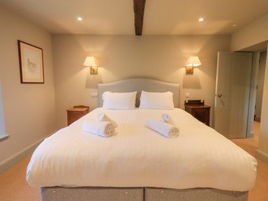 A bedroom with a large bed with white bedding and rolled towels on top at Green Yew in Winster near Bowness-On-Windermere