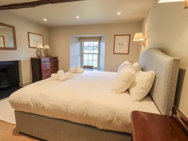 A bedroom with a large bed and white bedding a chest of drawers and a window at Green Yew Winster near Bowness-On-Windermere