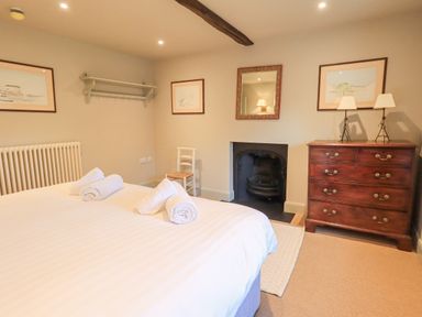 A bedroom with a bed and rolled towels a wooden chest of drawers a chair and a fireplace at Green Yew in Winster near Bowness-On-Windermere