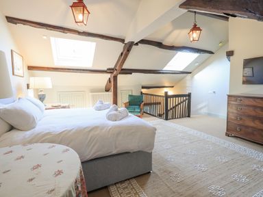 A bedroom with a bed, a dresser, an armchair, skylights, and exposed wooden beams at Green Yew Winster near Bowness-On-Windermere