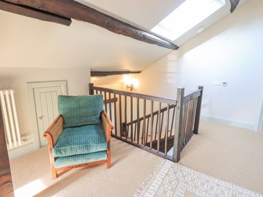 An upstairs landing with a green upholstered armchair near wooden stairs and exposed ceiling beams at Green Yew in Winster near Bowness-On-Windermere