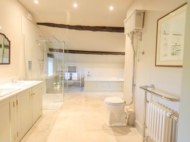 A bathroom with a toilet a shower a bathtub a double sink vanity and exposed wooden beams at Green Yew in Winster near Bowness-On-Windermere