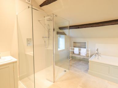 A bathroom with a glass shower enclosure a bathtub a towel rack and exposed wooden beams at Green Yew in Winster near Bowness-On-Windermere
