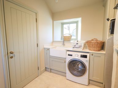 A laundry room with a washing machine sink baskets and cabinets at Green Yew in Winster near Bowness-On-Windermere