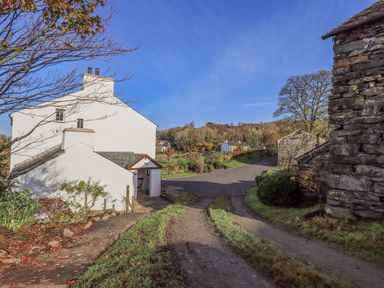 A rural road with white houses and stone buildings surrounded by trees and grass at Green Yew Winster near Bowness-On-Windermere