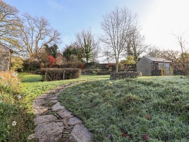 A garden with a stone pathway leading to a tree surrounded by a stone wall and a small shed at Green Yew in Winster near Bowness-On-Windermere