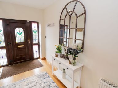 An entryway with a wooden door featuring stained glass panels a white console table with flowers and decorative items and a large arched mirror on the wall at Doonalton House in Dromore West County Sligo