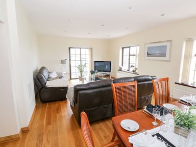 A living room with brown leather sofas facing a television and a dining table with plates and glasses at Doonalton House in Dromore West County Sligo