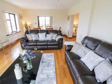 A living room with two black leather sofas with pillows and a glass coffee table with flowers at Doonalton House in Dromore West County Sligo