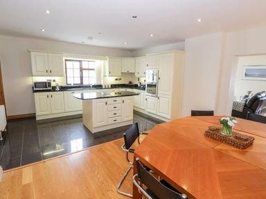 A kitchen with white cabinets a black countertop a kitchen island and a wooden dining table with black chairs at Doonalton House in Dromore West County Sligo