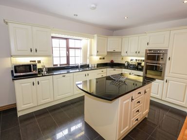 A kitchen with white cabinets black countertops a central island oven microwave and a window at Doonalton House in Dromore West County Sligo