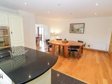 A dining area with a wooden table and black chairs adjacent to a kitchen with a black countertop at Doonalton House in Dromore West County Sligo