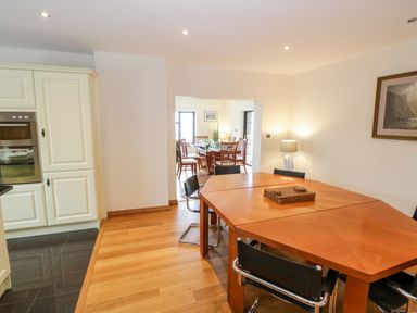 A dining area with a wooden table and black chairs next to a kitchen with cream cabinets and an oven at Doonalton House in Dromore West County Sligo