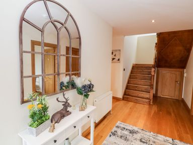 A hallway with wooden stairs a white console table with decorative items and a large windowpane mirror on the wall at Doonalton House in Dromore West County Sligo