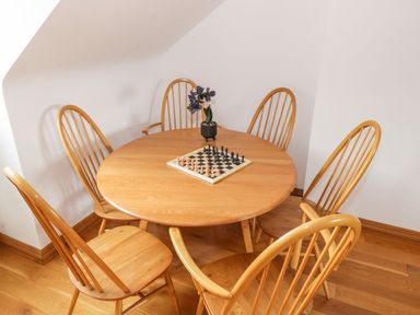 A wooden round dining table with six wooden chairs a chessboard and a small black flower pot on the table at Doonalton House in Dromore West County Sligo