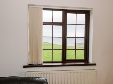 A window with beige vertical blinds overlooking green grass and a body of water at Doonalton House in Dromore West County Sligo